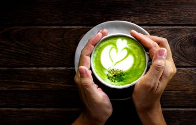 Women’s Hand holding cup of matcha Latte on old Wooden Background table, Green Tea on old Wooden Background table