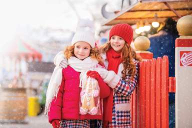 Children of red-haired sisters walk at a festively decorated Christmas market in the city.