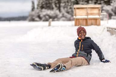 Boy wearing ice skate sits and laughs on ice after falling