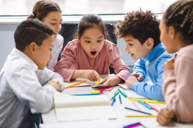 Diverse small schoolchildren using phone at classroom